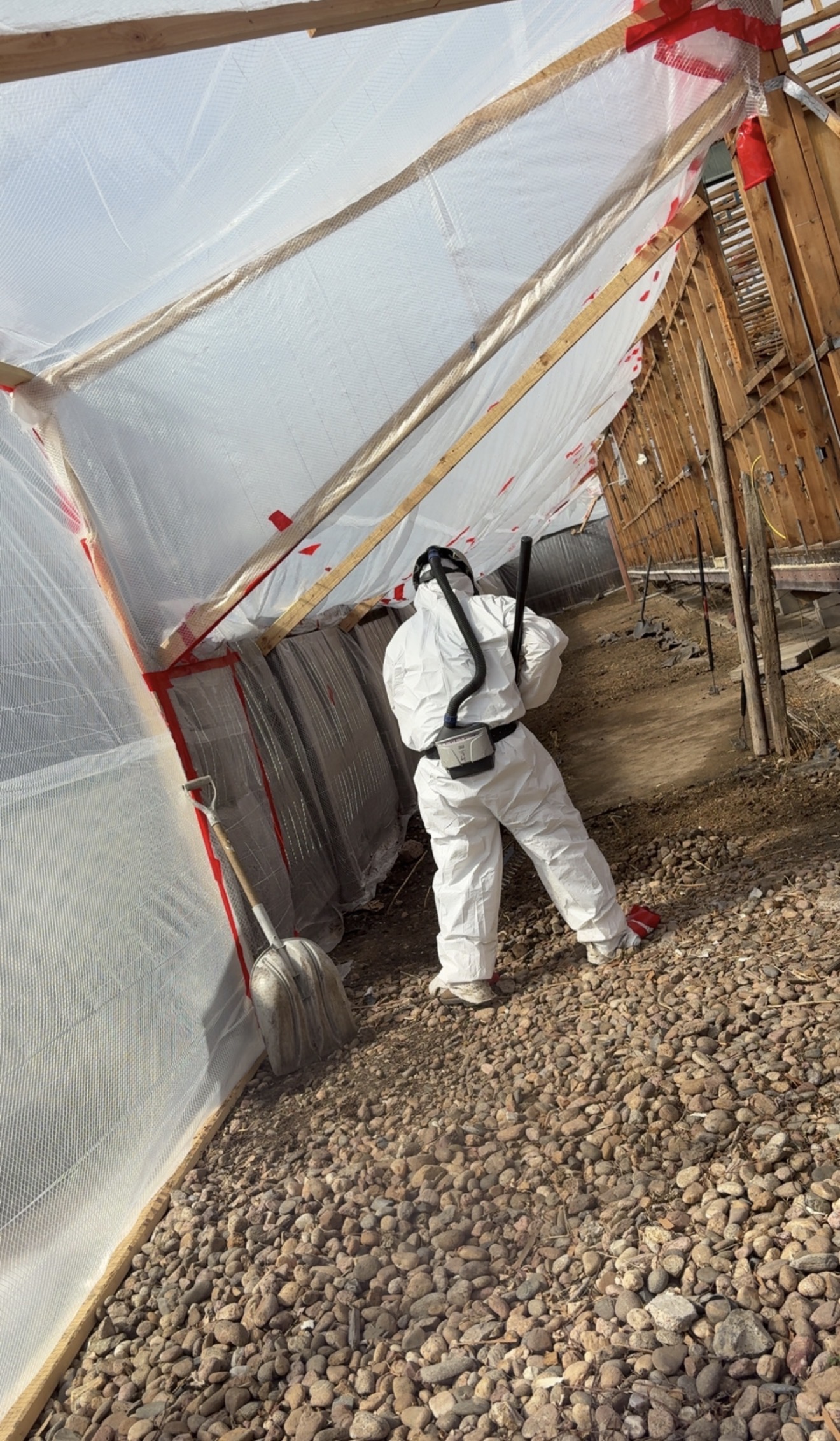 Worker in full Tyvek suit and powered air-purifying respirator entering an exterior asbestos containment