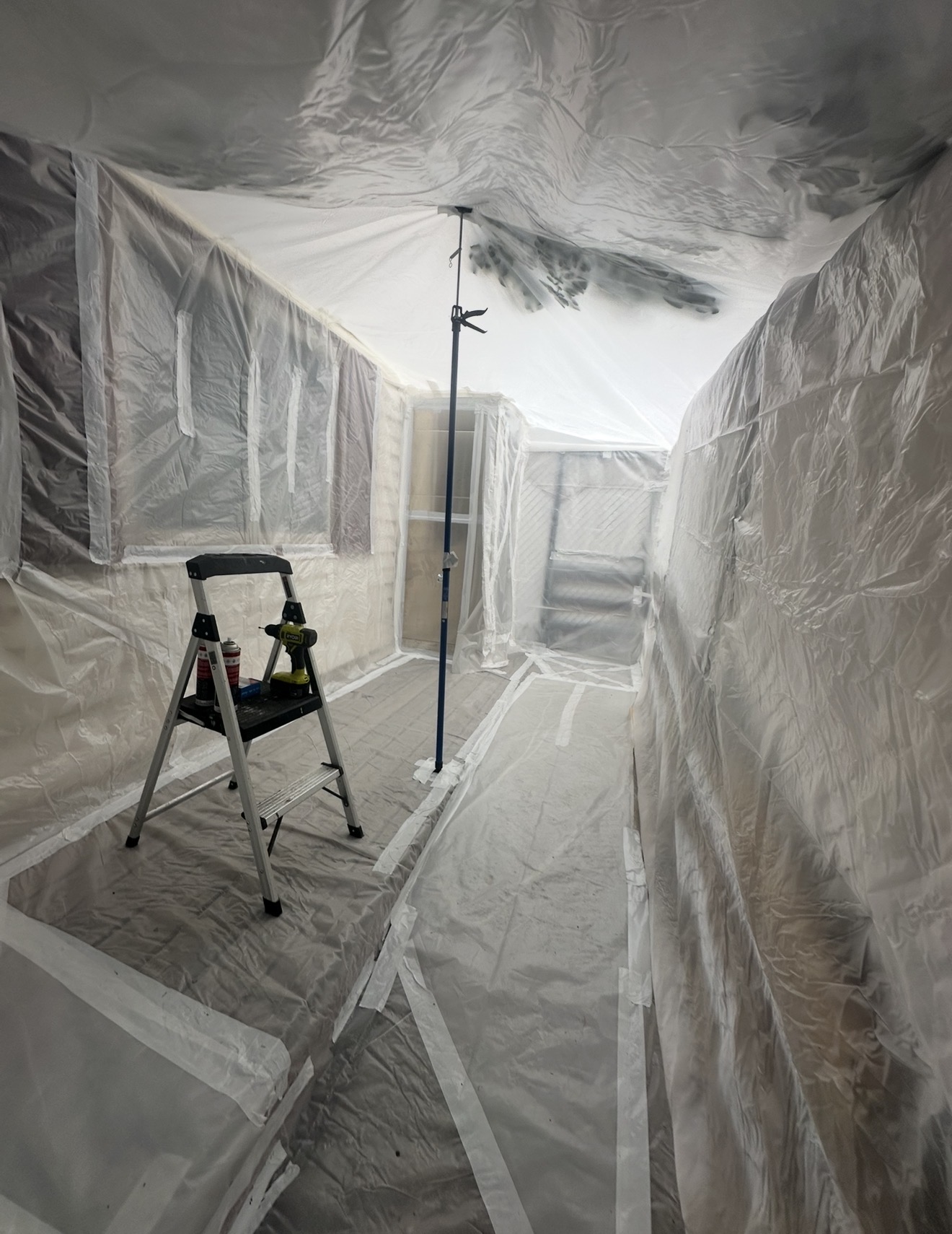 Interior poly-wrapped containment with step ladder, drill, and tools staged for active abatement