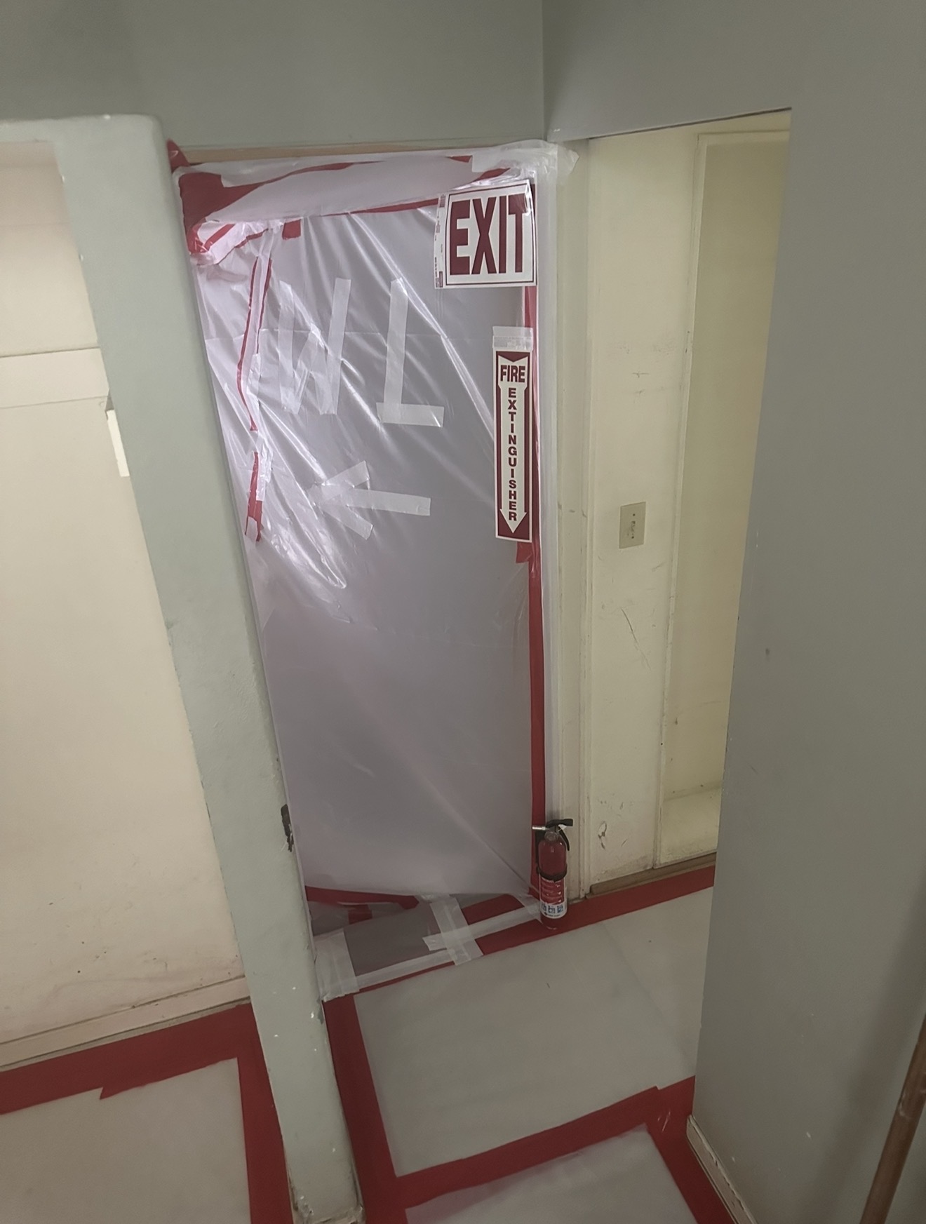 Sealed interior doorway wrapped in poly with EXIT and Fire Extinguisher signage during active asbestos containment