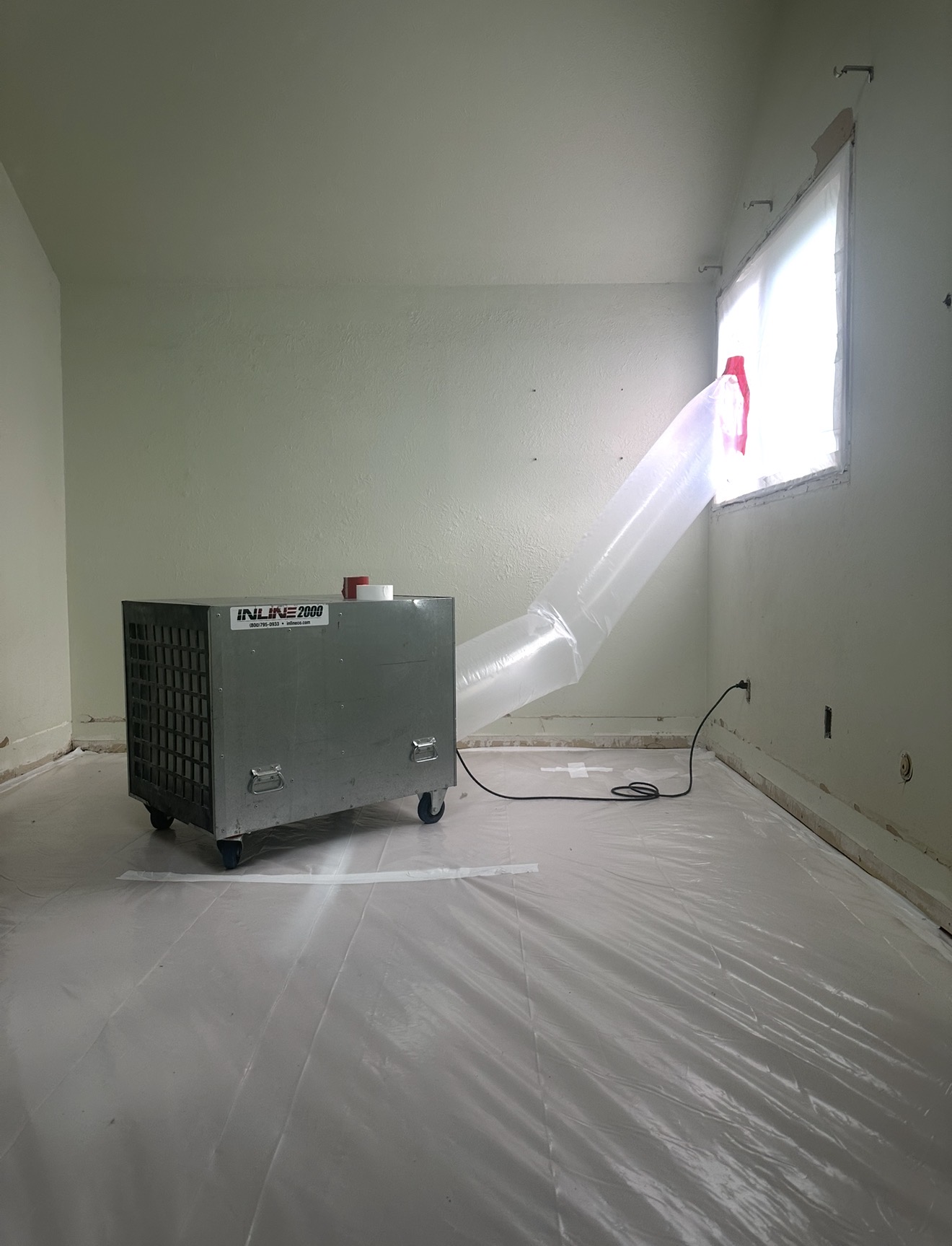 Negative-air machine ducting through a sealed window in a poly-wrapped abatement work area