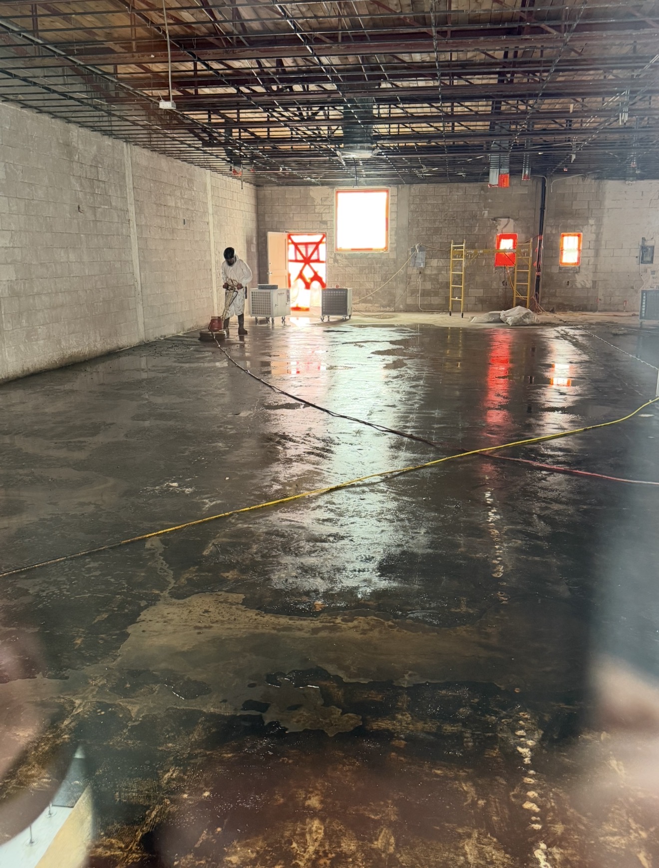 Worker in full PPE pressure washing a concrete warehouse floor after asbestos floor tile removal