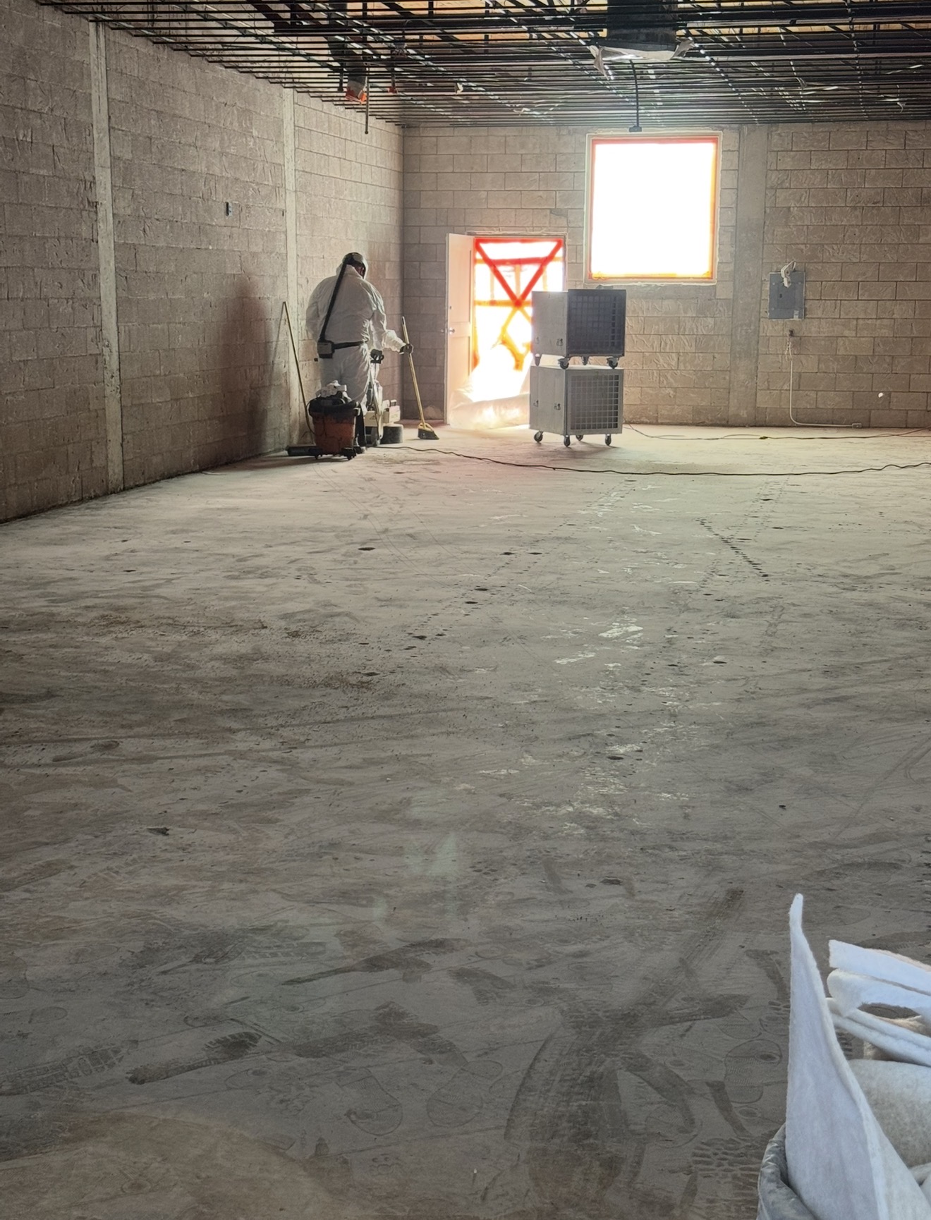 Technician in PPE doing final wet wipe-down of a stripped commercial interior during clearance prep