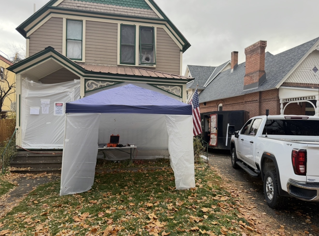 Historic Victorian home with full exterior poly containment, decon tent, and I&F Abatement Experts branded truck and trailer staged out front