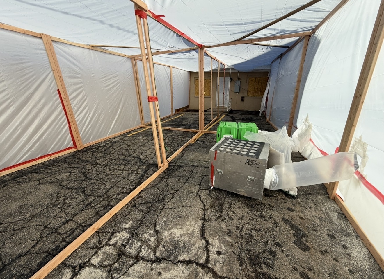 Wood-framed exterior decontamination chamber wrapped in clear poly on a paved job site