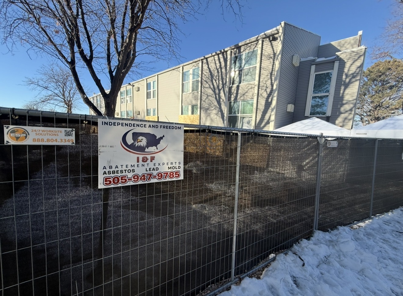 I&F Abatement Experts job-site sign mounted on temporary fencing in front of a fenced apartment-complex project
