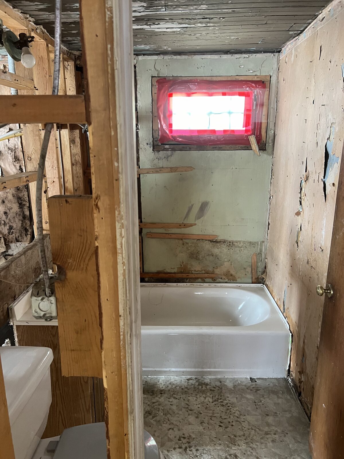 Empty room stripped to studs and subfloor with sealed window during active abatement