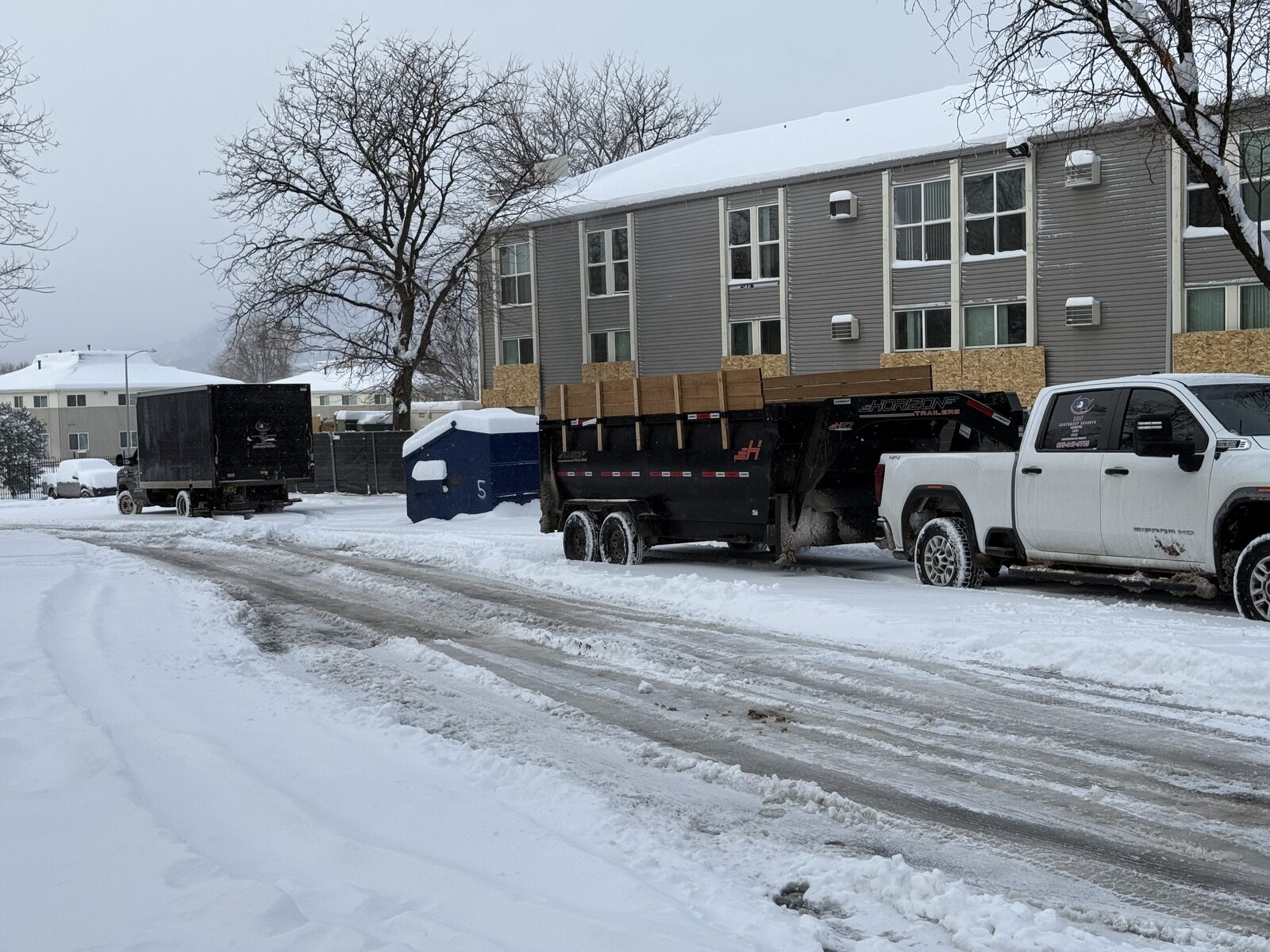 I&F Abatement Experts truck and dump trailer hauling debris away from a snow-covered apartment building